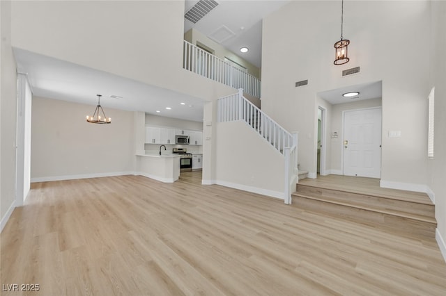 4132 Joyous St, North Las Vegas, NV 89032 - unfurnished living room with a towering ceiling, a chandelier, light wood-style flooring, baseboards, and a sink
