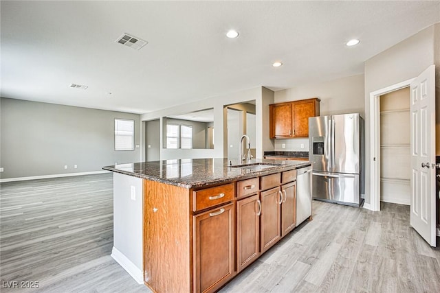 9271 Martel Ave, Las Vegas, NV 89148 - kitchen featuring appliances with stainless steel finishes, light wood-style floors, a sink, a center island with sink, and dark stone counters