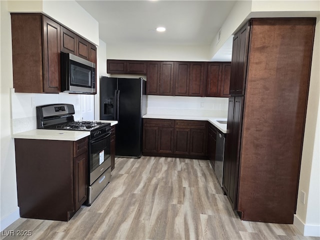 3056 Garnet Ct, Las Vegas, NV 89121 - kitchen featuring stainless steel microwave, gas range oven, black fridge, light wood-style floors, and dark brown cabinets