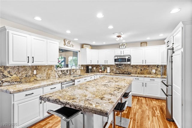 7545 Constantinople Ave, Las Vegas, NV 89129 - kitchen with stainless steel appliances, a sink, light wood-style flooring, white cabinets, and a kitchen island