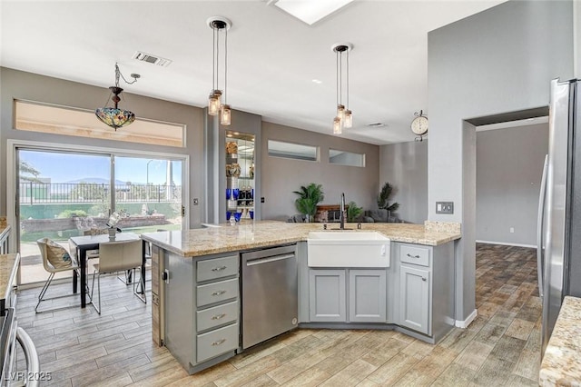 3112 Haddon Dr, Las Vegas, NV 89134 - kitchen featuring gray cabinetry, stainless steel appliances, light wood finished floors, light stone counters, and hanging light fixtures
