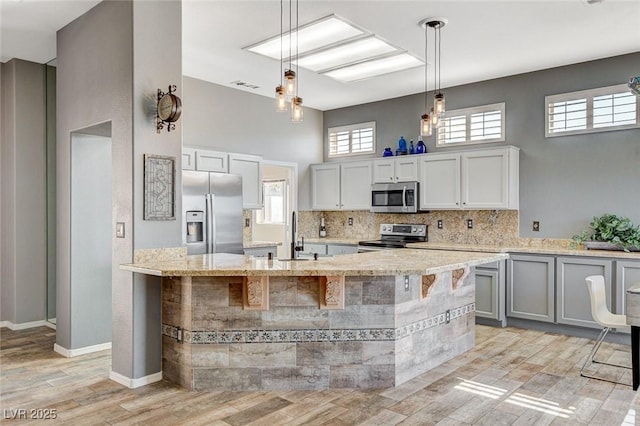 3112 Haddon Dr, Las Vegas, NV 89134 - kitchen featuring appliances with stainless steel finishes, light wood-style floors, tasteful backsplash, light stone counters, and decorative light fixtures