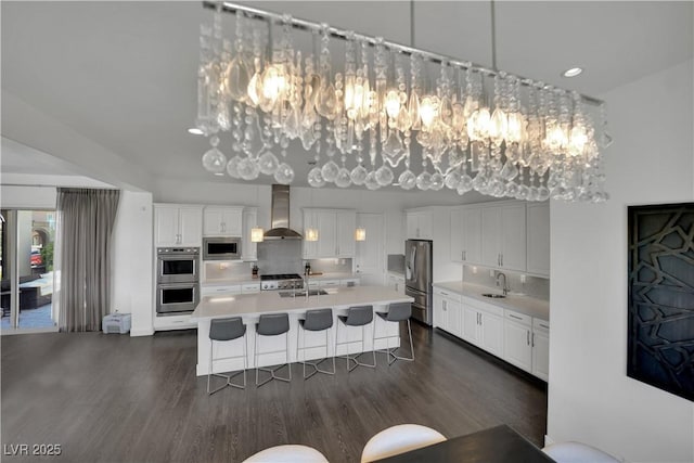 362 Port Reggio St, Las Vegas, NV 89138 - kitchen featuring wall chimney exhaust hood, appliances with stainless steel finishes, a sink, a chandelier, and dark wood-style flooring