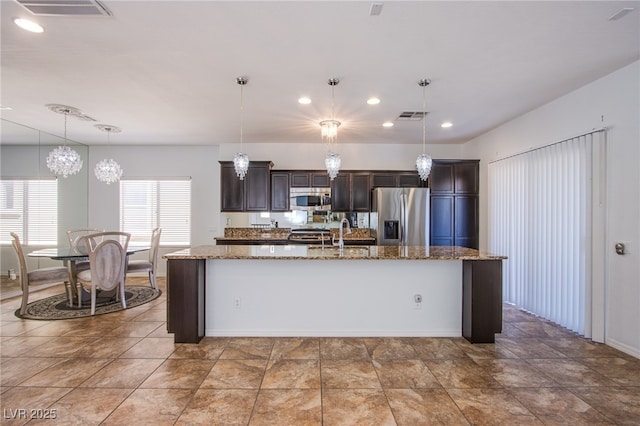 1794 Morro Vista Dr, Las Vegas, NV 89135 - kitchen featuring appliances with stainless steel finishes, dark brown cabinets, an island with sink, light stone countertops, and hanging light fixtures