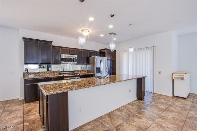 1794 Morro Vista Dr, Las Vegas, NV 89135 - kitchen with stainless steel appliances, dark brown cabinetry, a center island with sink, dark stone countertops, and decorative light fixtures