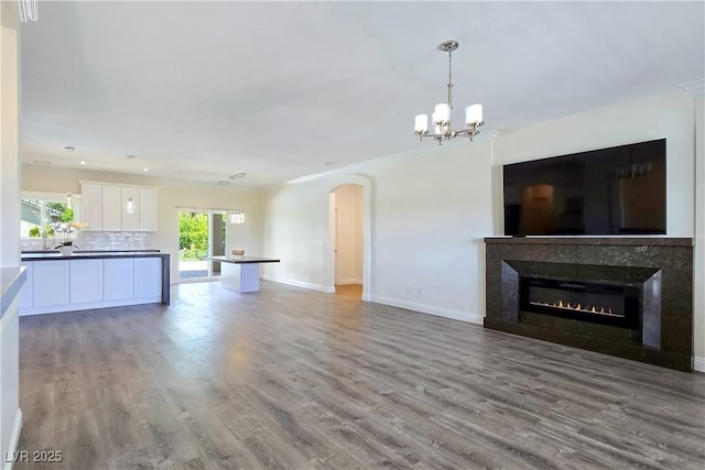 5500 Santovito St, Pahrump, NV 89061 - unfurnished living room with wood finished floors, baseboards, a chandelier, arched walkways, and a glass covered fireplace