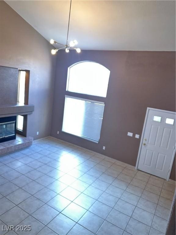 1511 Balsam Mist Ave, Las Vegas, NV 89183 - unfurnished living room featuring light tile patterned floors, a glass covered fireplace, high vaulted ceiling, and a chandelier