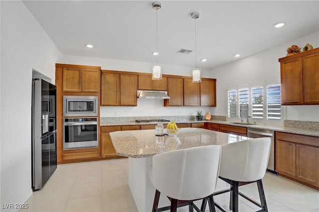 7255 Bold Rock Ave, Las Vegas, NV 89113 - kitchen featuring appliances with stainless steel finishes, a sink, under cabinet range hood, brown cabinetry, and a breakfast bar area