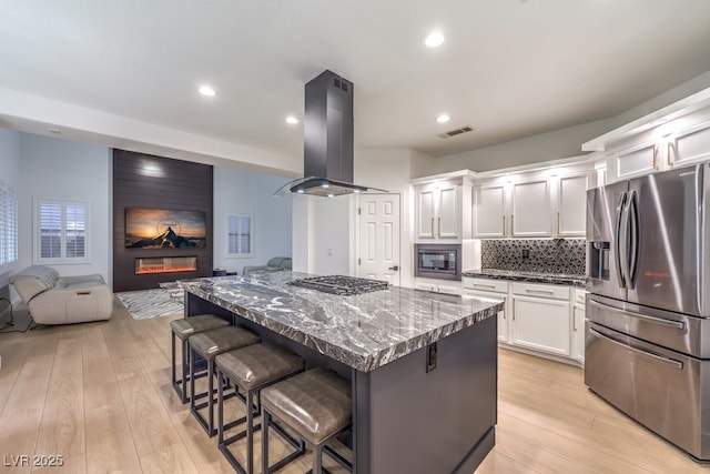 722 Descartes Ave, Henderson, NV 89002 - kitchen featuring stainless steel appliances, island range hood, open floor plan, a fireplace, and white cabinetry