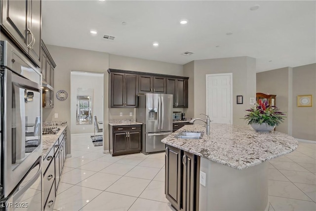 3155 Dalmazia Ave, Henderson, NV 89044 - kitchen with appliances with stainless steel finishes, a sink, light tile patterned flooring, dark brown cabinetry, and a center island with sink