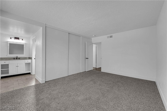 6791 Greengrove Dr, Las Vegas, NV 89103 - unfurnished bedroom featuring a sink, a textured ceiling, a closet, connected bathroom, and light carpet