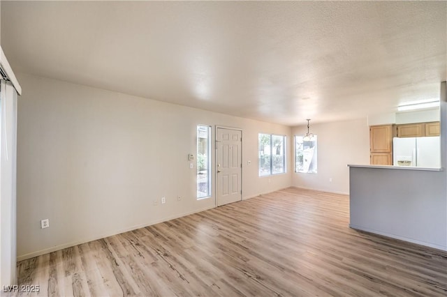 5710 E Tropicana Ave Unit 1114, Las Vegas, NV 89122 - unfurnished living room with a chandelier, light wood-style floors, and baseboards