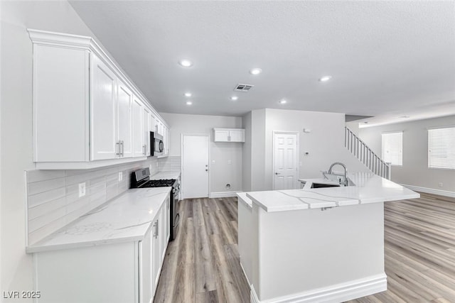 9766 Marcelline Ave, Las Vegas, NV 89148 - kitchen with stainless steel appliances, light wood-style floors, white cabinets, tasteful backsplash, and an island with sink
