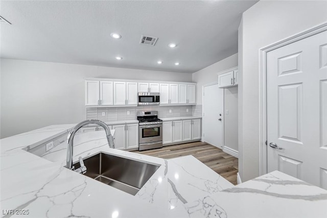 9766 Marcelline Ave, Las Vegas, NV 89148 - kitchen with stainless steel appliances, a sink, light wood-style floors, backsplash, and white cabinets