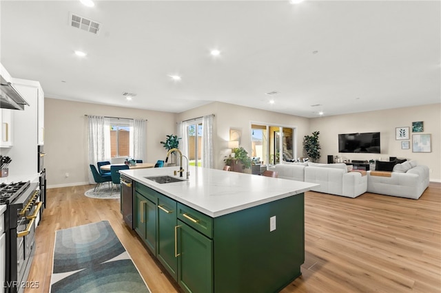 10906 Mila Landing Ave, Las Vegas, NV 89166 - kitchen featuring green cabinets, a sink, stainless steel appliances, light wood-type flooring, and a center island with sink