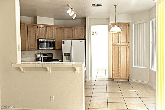 1721 Mill Canyon Dr, Las Vegas, NV 89128 - kitchen featuring appliances with stainless steel finishes, tile counters, a peninsula, a breakfast bar, and light tile patterned floors