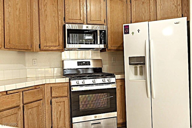 1721 Mill Canyon Dr, Las Vegas, NV 89128 - kitchen featuring stainless steel appliances, tile counters, backsplash, and brown cabinets