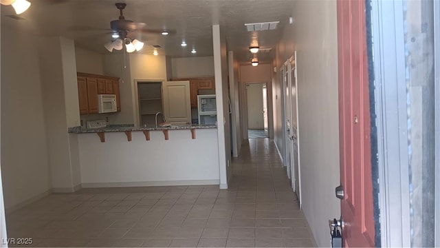 864 Chianti Way, Mesquite, NV 89027 - kitchen featuring white microwave, a ceiling fan, light tile patterned flooring, a kitchen breakfast bar, and baseboards