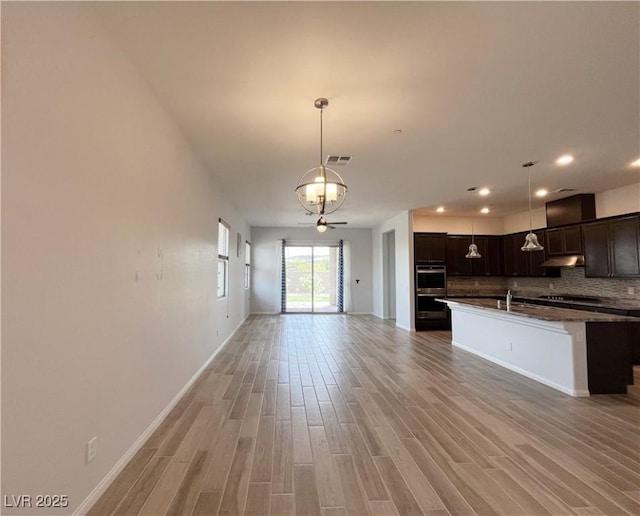 12565 Huckleberry Oak Ave, Las Vegas, NV 89138 - kitchen featuring open floor plan, decorative backsplash, light wood finished floors, under cabinet range hood, and dark brown cabinetry