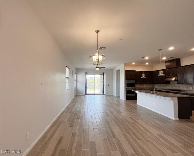 12565 Huckleberry Oak Ave, Las Vegas, NV 89138 - kitchen featuring open floor plan, backsplash, light wood finished floors, under cabinet range hood, and dark brown cabinets