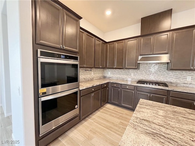 12565 Huckleberry Oak Ave, Las Vegas, NV 89138 - kitchen with appliances with stainless steel finishes, under cabinet range hood, dark brown cabinets, tasteful backsplash, and light stone countertops