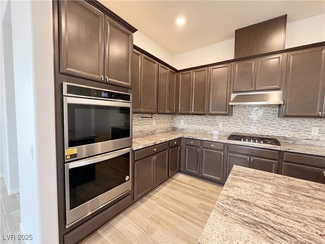 12565 Huckleberry Oak Ave, Las Vegas, NV 89138 - kitchen featuring stainless steel appliances, under cabinet range hood, dark brown cabinetry, backsplash, and light stone counters