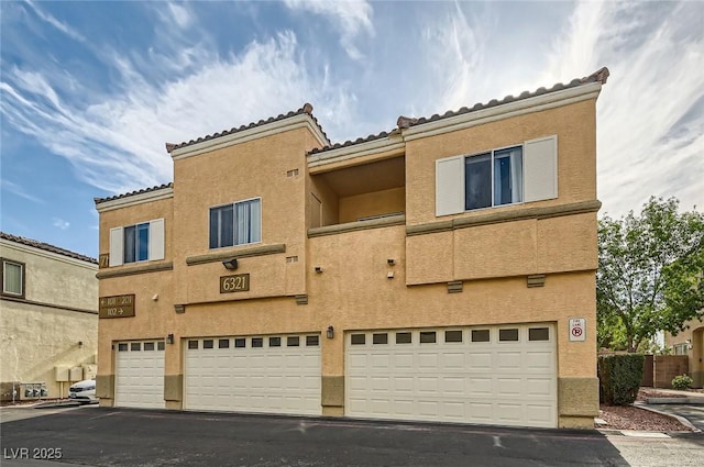 6321 Rolling Rose St Unit 201, North Las Vegas, NV 89081 - back of house featuring a garage, stucco siding, asphalt driveway, and a tiled roof