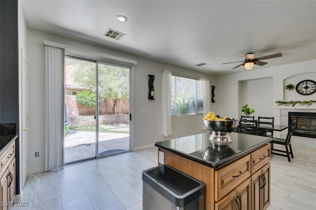 11004 Napa Ridge Dr, Las Vegas, NV 89144 - kitchen featuring brown cabinets, a glass covered fireplace, a ceiling fan, baseboards, and dark stone countertops