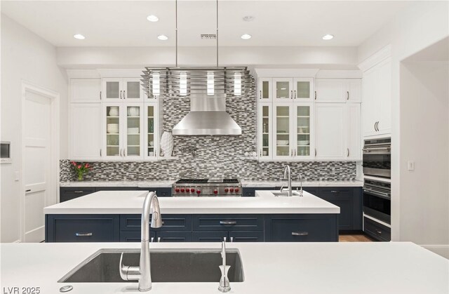 11 Misty Peaks Ct, Las Vegas, NV 89135 - kitchen featuring wall chimney range hood, a center island with sink, white cabinetry, tasteful backsplash, and light countertops