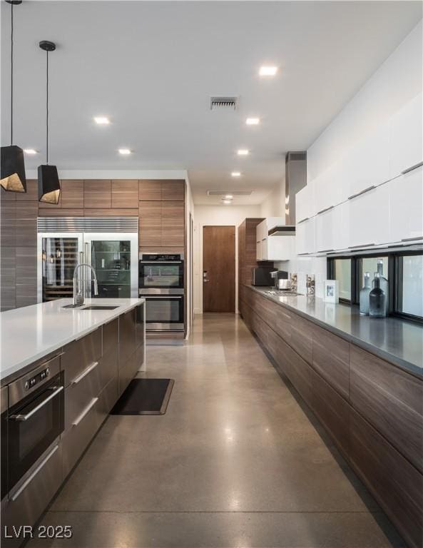 7030 Schirlls St, Las Vegas, NV 89118 - kitchen with modern cabinets, wall chimney exhaust hood, finished concrete floors, stainless steel appliances, and hanging light fixtures