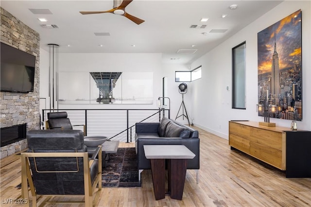 7030 Schirlls St, Las Vegas, NV 89118 - living room featuring light wood-style flooring, a ceiling fan, a stone fireplace, and baseboards