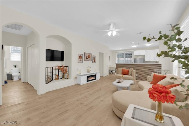 2633 Spider Cactus Ct, Las Vegas, NV 89106 - living area with light wood-style flooring, ceiling fan, arched walkways, and a warm lit fireplace