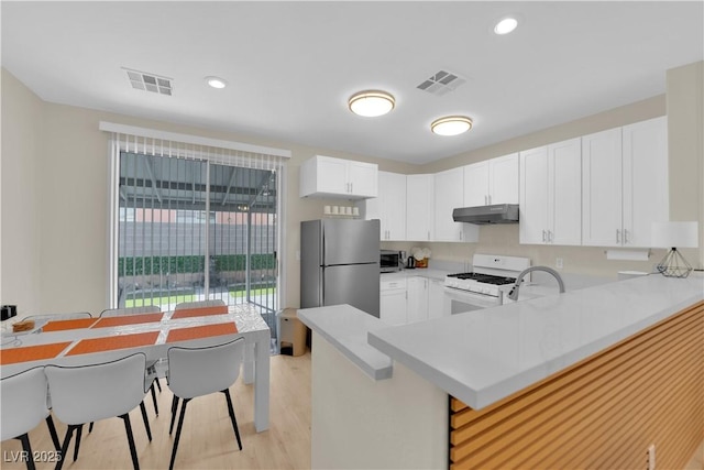 2633 Spider Cactus Ct, Las Vegas, NV 89106 - kitchen featuring under cabinet range hood, white gas stove, freestanding refrigerator, a peninsula, and light countertops