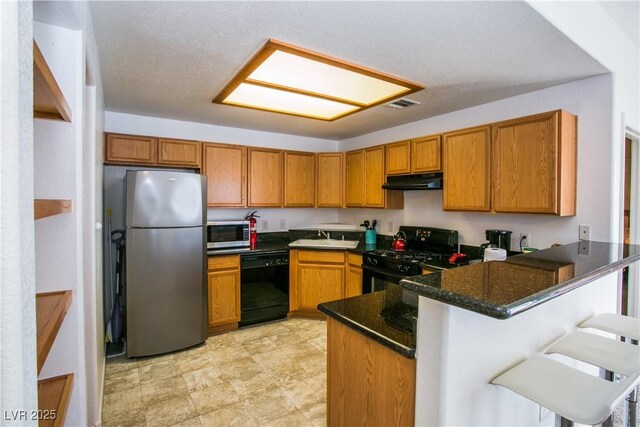 4655 Gold Dust Ave Unit 206, Las Vegas, NV 89120 - kitchen with black appliances, under cabinet range hood, a peninsula, brown cabinets, and dark stone counters