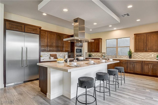 10228 Shell Star Ave, Las Vegas, NV 89135 - kitchen featuring built in appliances, island range hood, a spacious island, a kitchen breakfast bar, and tasteful backsplash