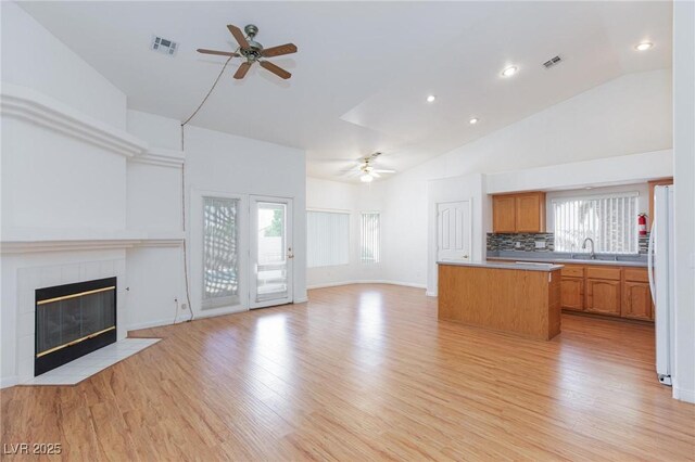 9091 W Viking Rd, Las Vegas, NV 89147 - unfurnished living room featuring a ceiling fan, a sink, light wood-style flooring, a tiled fireplace, and plenty of natural light