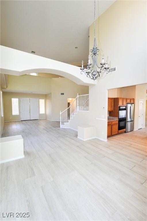 5808 Amber Station Ave, Las Vegas, NV 89131 - unfurnished living room with arched walkways, a towering ceiling, a chandelier, light wood-type flooring, and baseboards