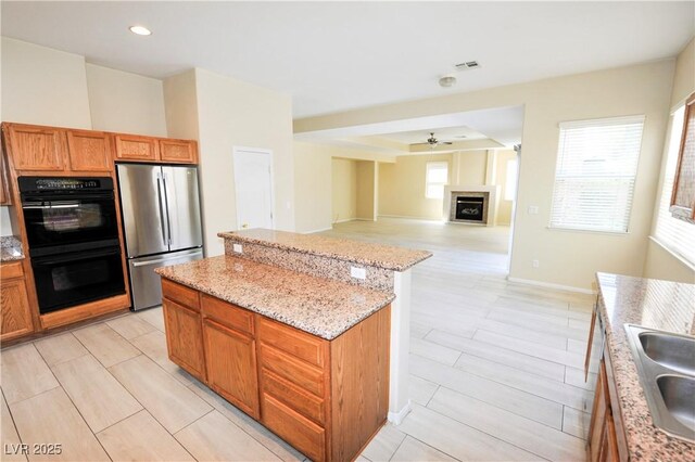 5808 Amber Station Ave, Las Vegas, NV 89131 - kitchen with freestanding refrigerator, a kitchen island, ceiling fan, a fireplace, and light stone countertops