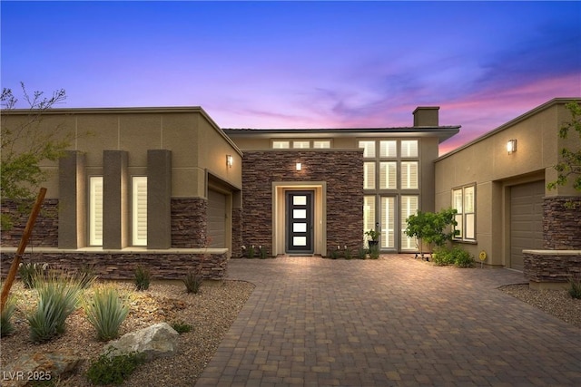 6700 Regency Stone Way, Las Vegas, NV 89148 - exterior entry at dusk with stone siding, stucco siding, an attached garage, and decorative driveway