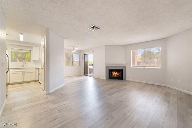 6871 Tamarus St Unit 204, Las Vegas, NV 89119 - unfurnished living room with a textured ceiling, plenty of natural light, light wood-style flooring, a fireplace with flush hearth, and a sink