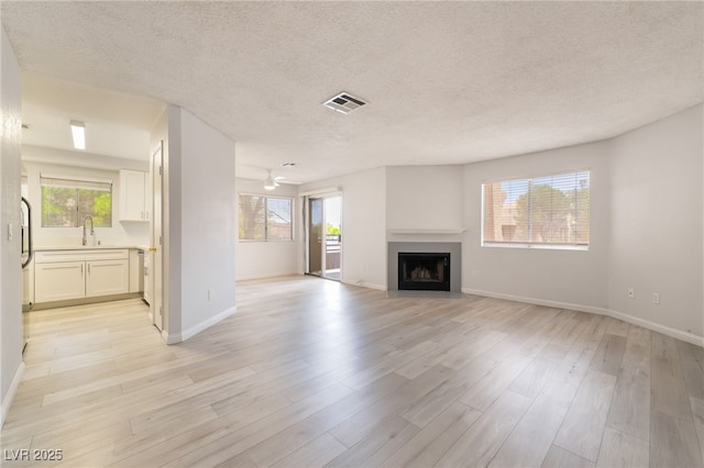 6871 Tamarus St Unit 204, Las Vegas, NV 89119 - unfurnished living room featuring light wood-style flooring, plenty of natural light, a textured ceiling, a sink, and a fireplace with flush hearth