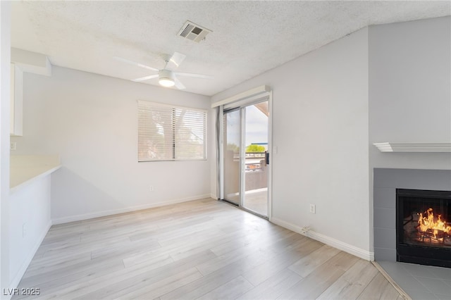 6871 Tamarus St Unit 204, Las Vegas, NV 89119 - unfurnished living room with light wood-style flooring, a textured ceiling, a ceiling fan, a fireplace with flush hearth, and baseboards