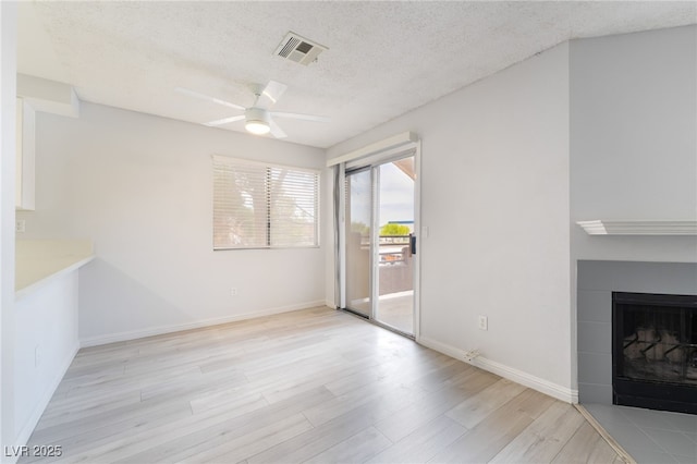 6871 Tamarus St Unit 204, Las Vegas, NV 89119 - unfurnished living room with light wood-style floors, a textured ceiling, a ceiling fan, baseboards, and a tiled fireplace
