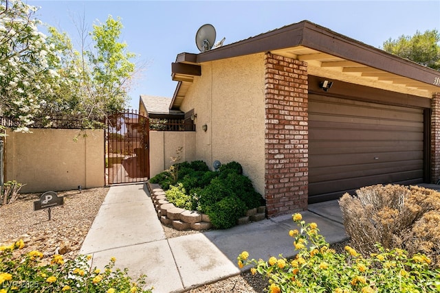 3890 Lancome St, Las Vegas, NV 89115 - view of side of home with a gate, an attached garage, stucco siding, and brick siding