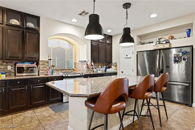 6714 Flamenco Ct, Las Vegas, NV 89139 - kitchen with stainless steel appliances, backsplash, light stone counters, dark brown cabinetry, and a breakfast bar