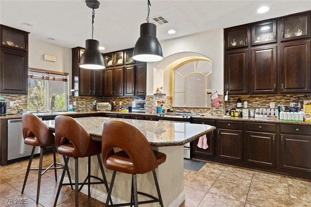 6714 Flamenco Ct, Las Vegas, NV 89139 - kitchen featuring stainless steel dishwasher, a breakfast bar area, tasteful backsplash, light stone counters, and dark brown cabinetry