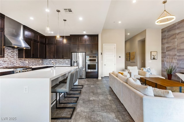 11672 Barga Ct, Las Vegas, NV 89138 - kitchen with stainless steel appliances, wall chimney range hood, dark brown cabinets, open floor plan, and light countertops