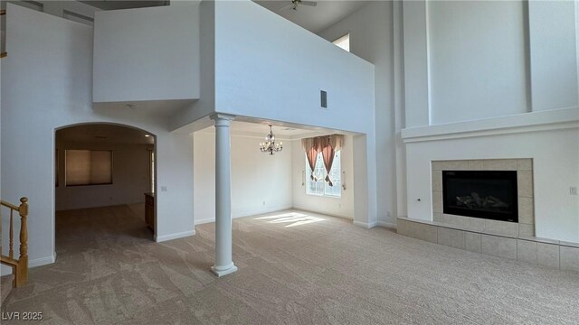 10066 Golden Bluff Ave, Las Vegas, NV 89148 - unfurnished living room featuring carpet, a high ceiling, arched walkways, a tiled fireplace, and a chandelier