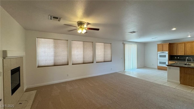 10066 Golden Bluff Ave, Las Vegas, NV 89148 - unfurnished living room with light carpet, a sink, a tiled fireplace, a ceiling fan, and light tile patterned floors
