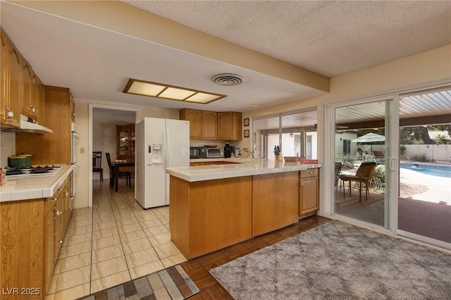 4219 E Pinecrest Cir, Las Vegas, NV 89121 - kitchen featuring white fridge with ice dispenser, tile counters, under cabinet range hood, a peninsula, and gas cooktop